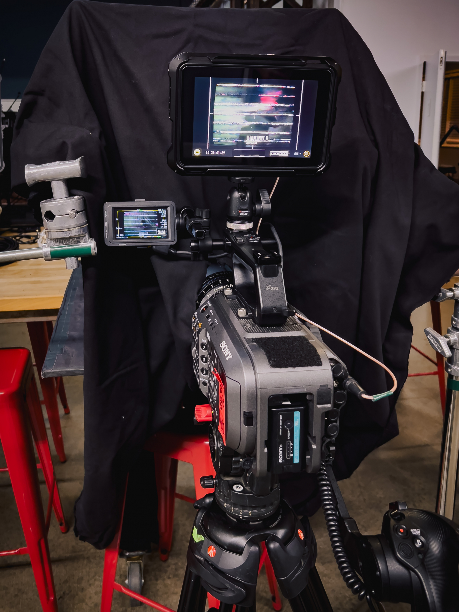 A camera on a tripod with the lens poking into a black curtain recording a CRT screen playing a VHS tape.